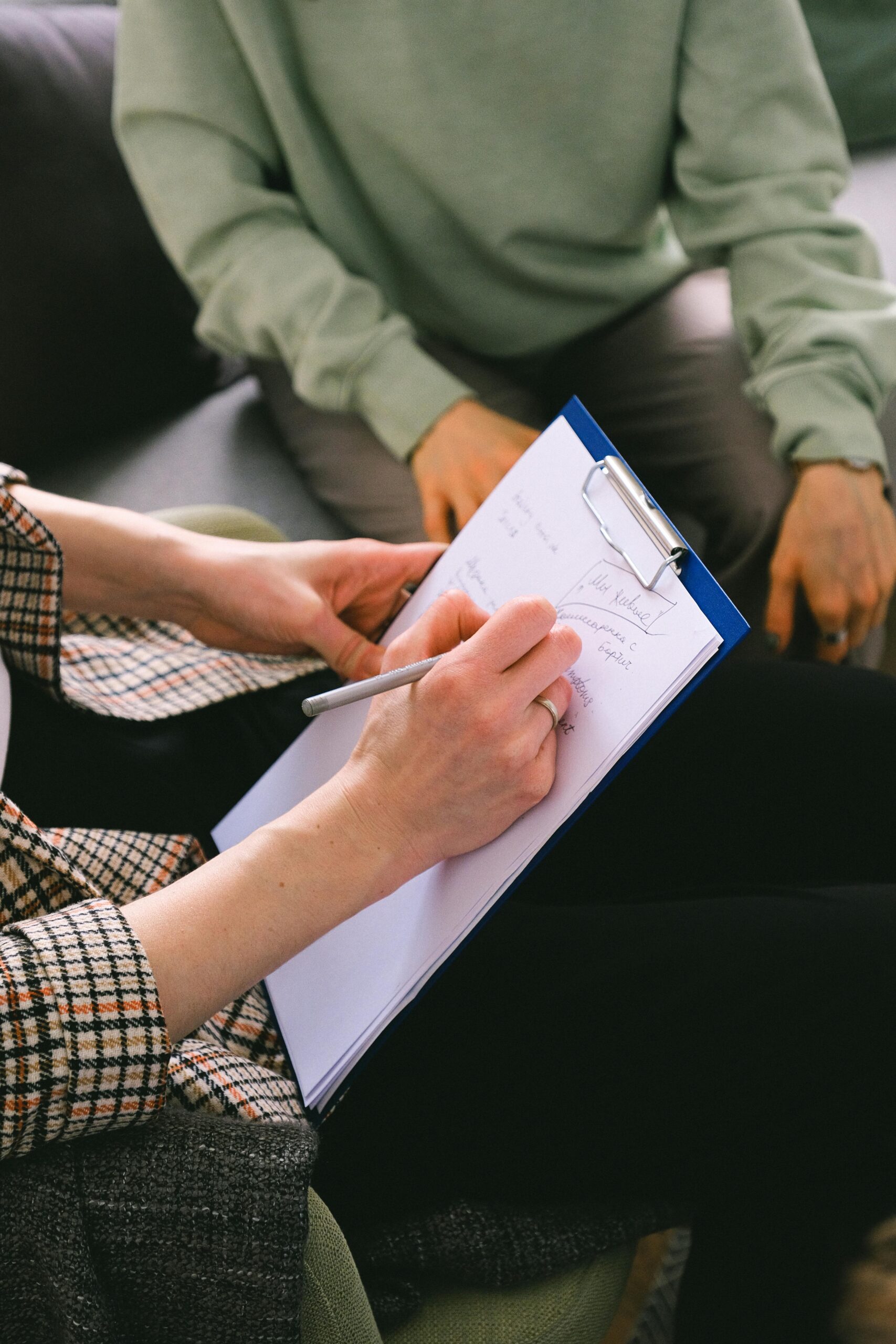 Crop anonymous female coach writing notes on paper in clipboard while talking with client in room